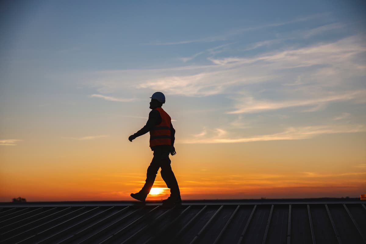 Trabajador caminando con total seguridad encima de un paso de gato y con un atardecer al fondo