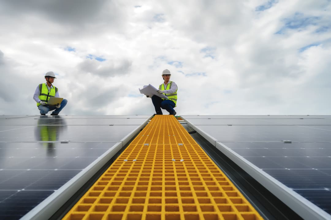 Ingenieros en el tejado industrial mientras analizan los paneles solares estando en un paso de gato