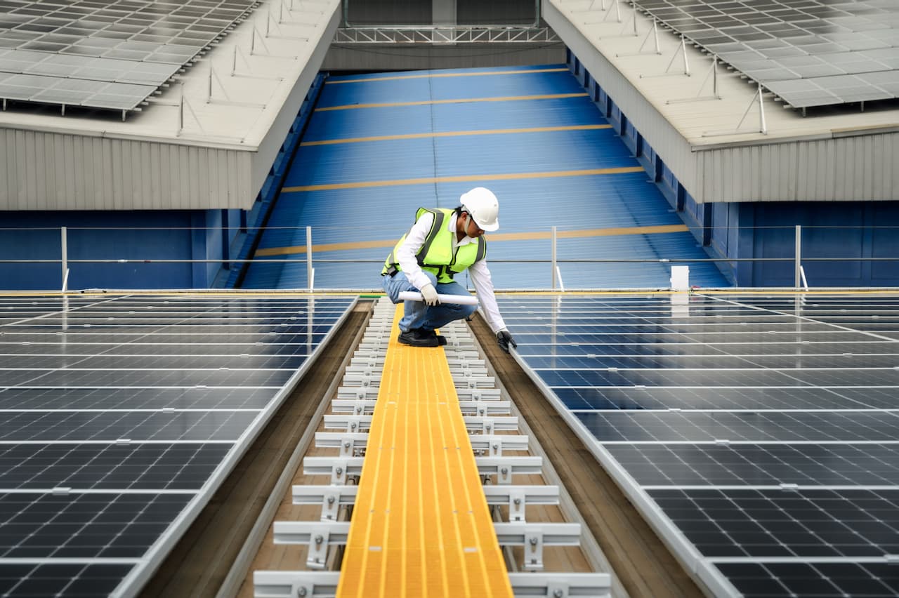 Trabajador tocando la estructura de un panel solar mientras esta agachado en un paso de gato